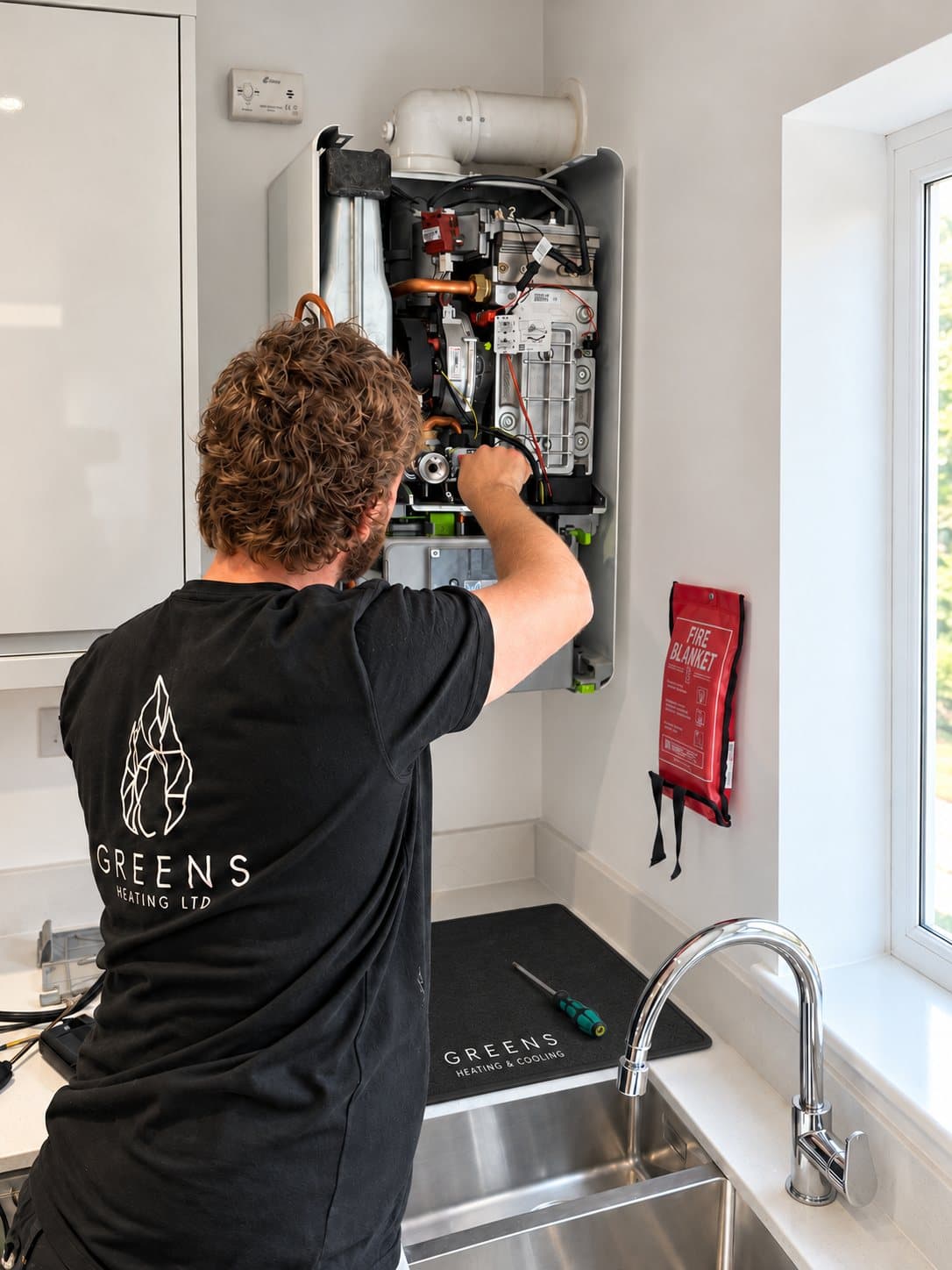 A Greens engineer working inside an open boiler in a kitchen